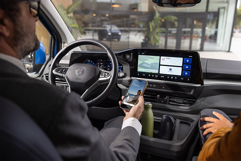 Mężczyzna siedzi w Volkswagenie trzymając smartfona w ręku.