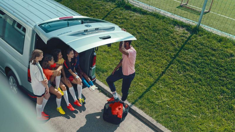 Einige Fußballerinnen sitzen im Kofferraum von einem Volkswagen Caravelle.