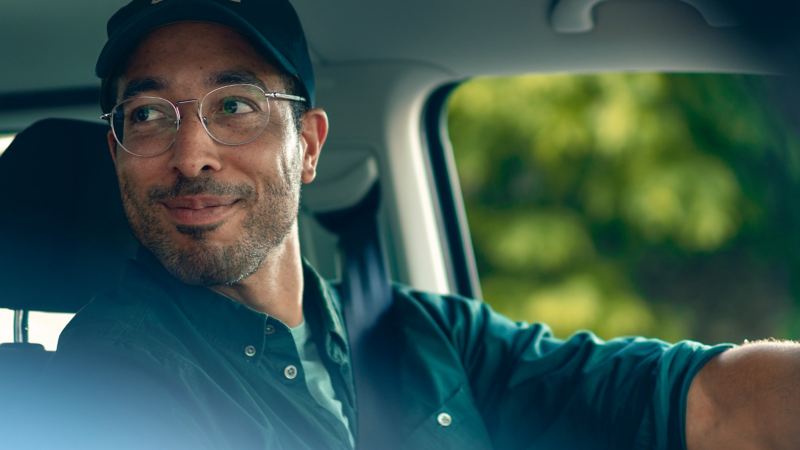 Un uomo siede al volante e guarda sorridendo oltre la sua spalla.