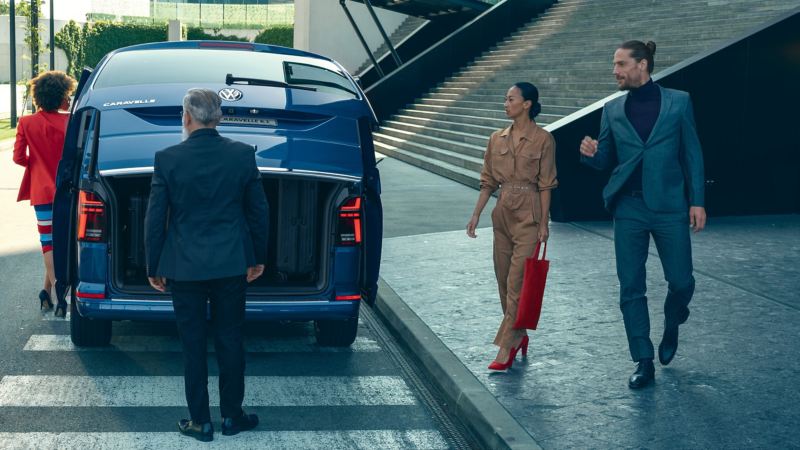 Cztery osoby stoją z tyłu Volkswagen Caravelle 6.1 z otwartą tylną klapą.