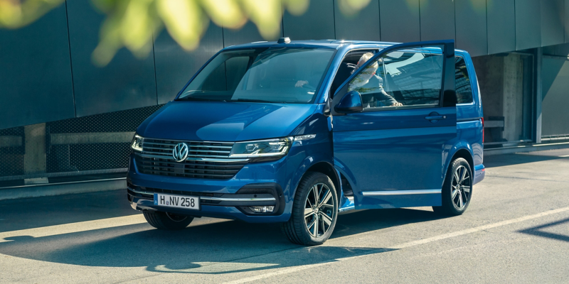 Ein VW Caravelle 6.1 schräg von der Seite. Ein Mann steigt in das Fahrzeug ein.