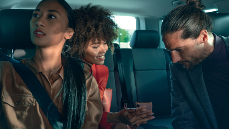 Un homme et deux femmes sont assis dans l’habitacle d’une Volkswagen et regardent un smartphone.