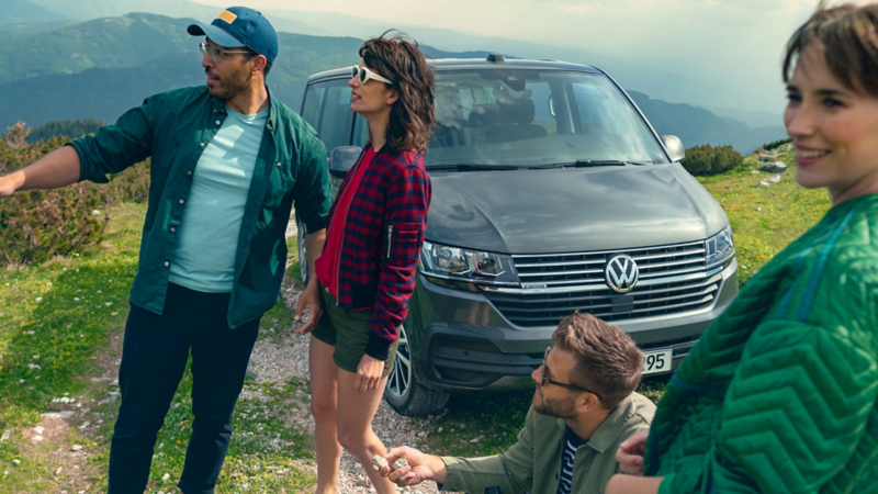 Tre ragazzi vicino a un VW Caravelle parcheggiato, vista frontale di 3/4.