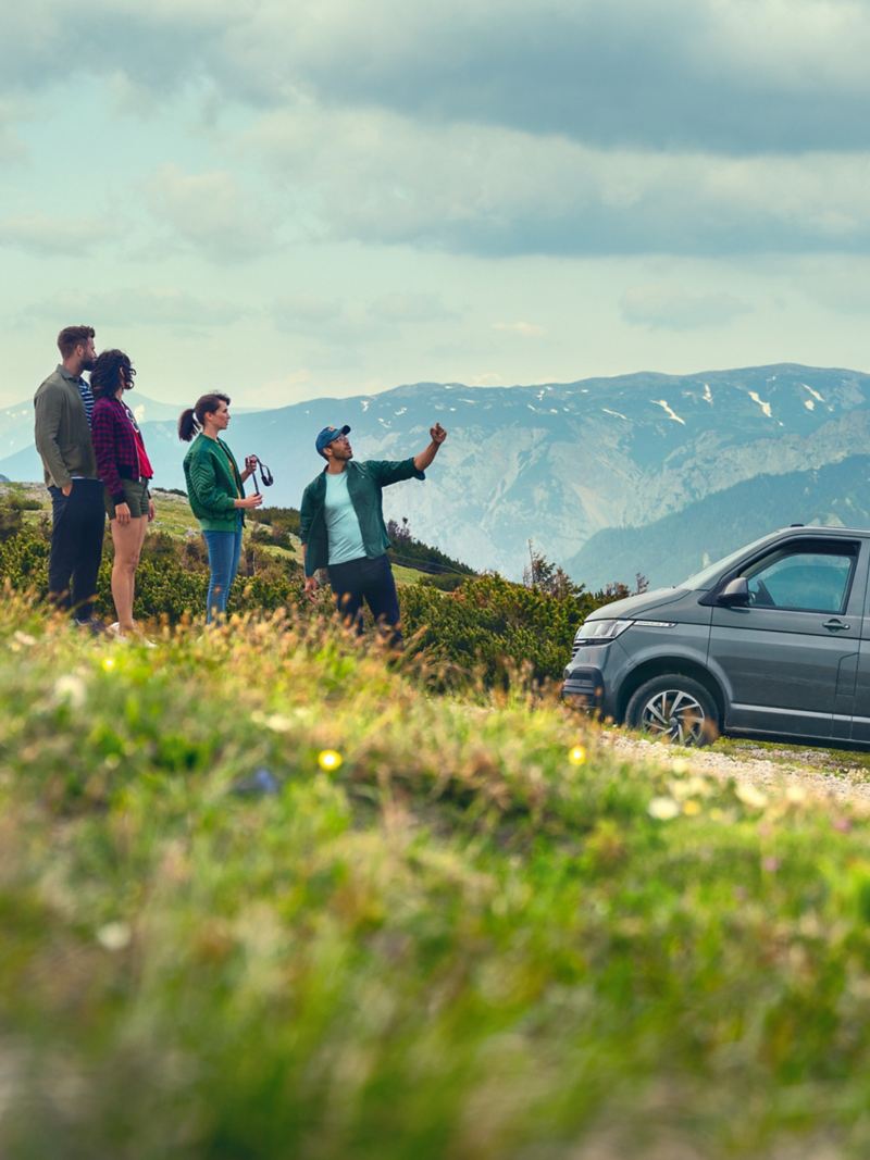 Grupa osób stoi przed Volkswagenem Caravelle w Alpach.