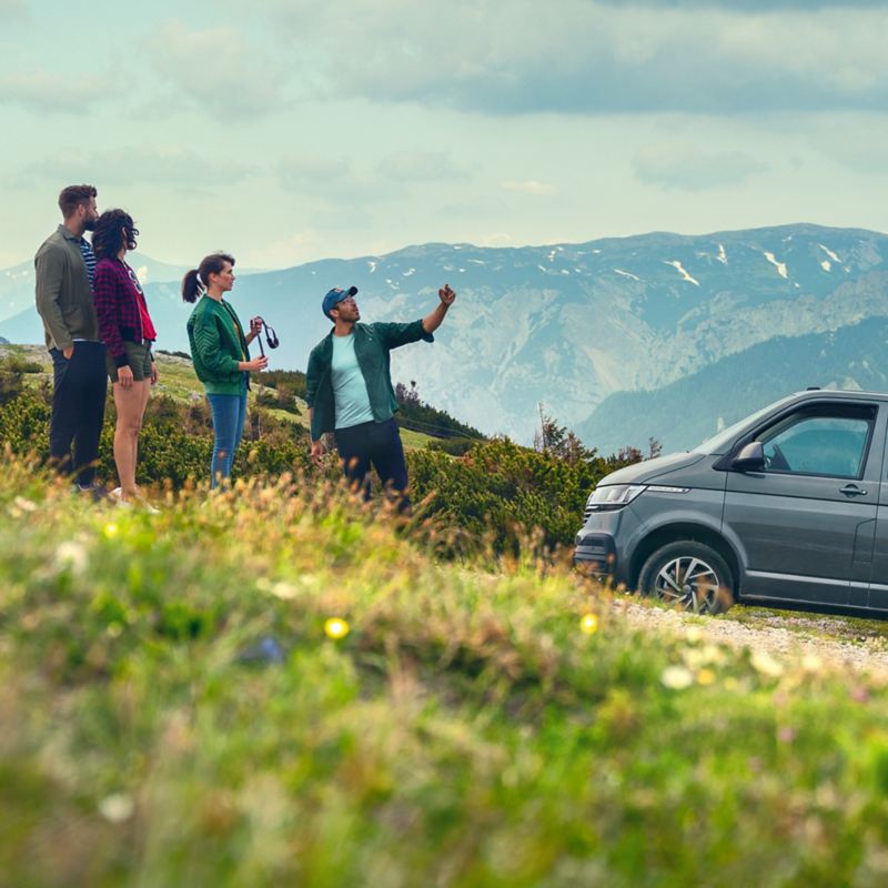 A group of people is standing in front of a Volkswagen Caravelle in the Alps.