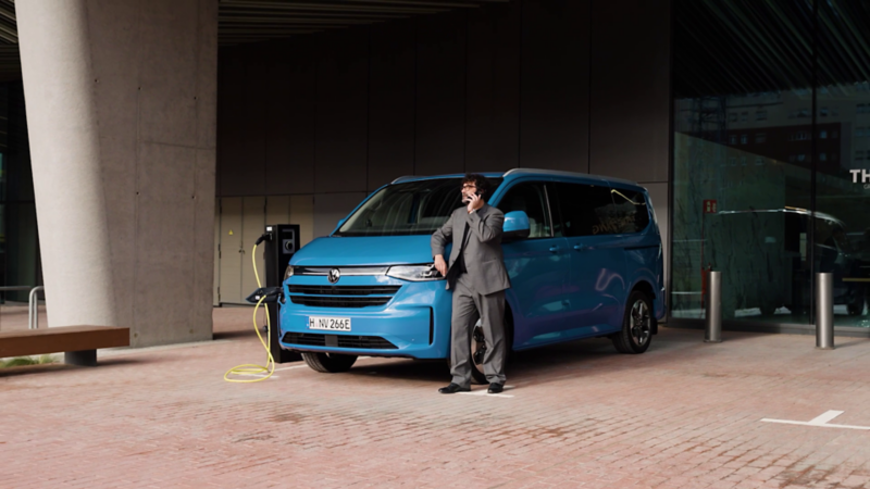 En blå VW Caravelle står parkerad vid en laddstolpe