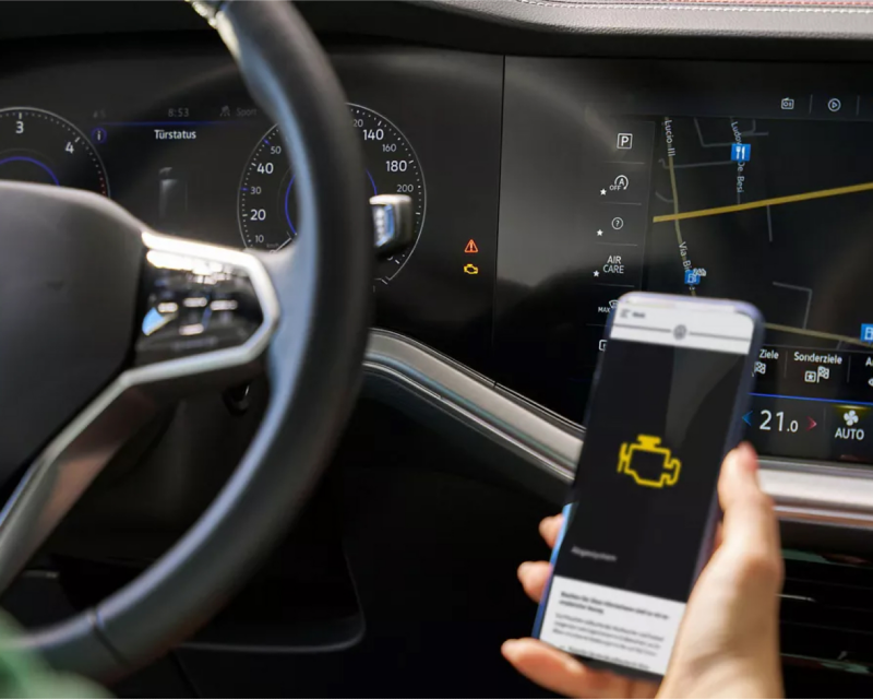 Mobile phone being held in front of VW vehicle interior with dashboard light showing on screen.