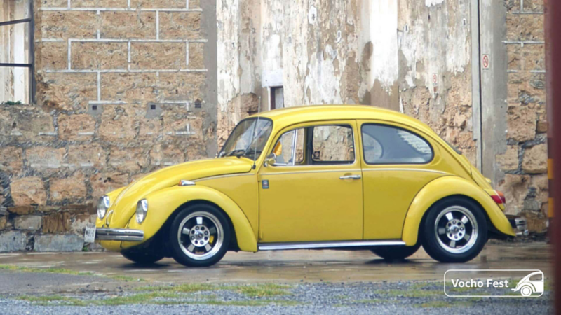 Vocho amarillo. Carro clásico de Volkswagen cerca de una construcción antigua.