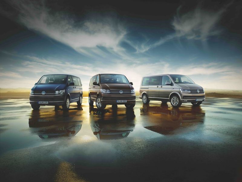 Trois fourgons VW, un Transporter, un Multivan et un Caravelle sont garés sur un parking au coucher du soleil