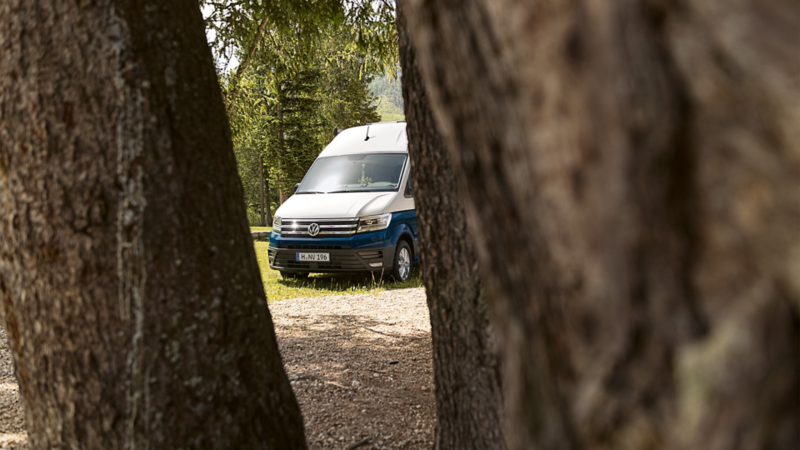 A VW Grand California stands between two trees.