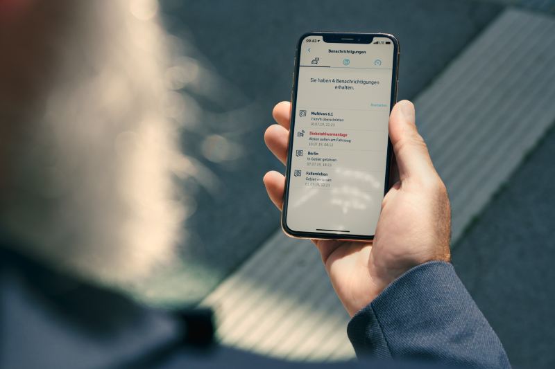 Mężczyzna patrzy na swojego smartfona z otwartą usługą Alarm antykradzieżowy online w aplikacji We Connect.