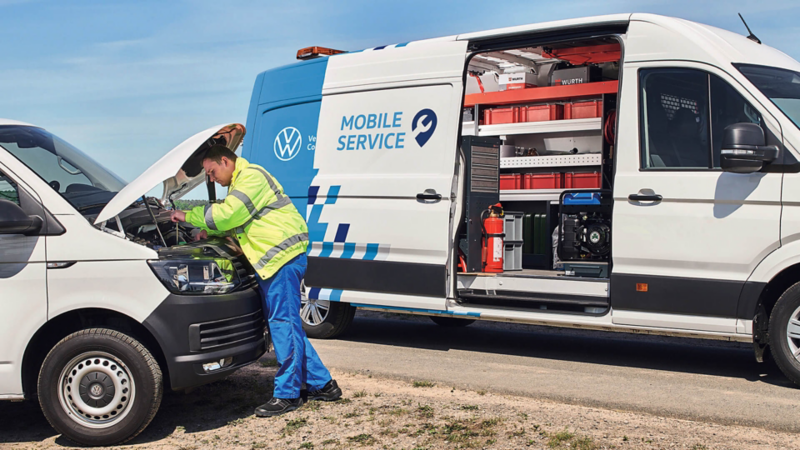 Un addetto a bordo strada ispeziona un veicolo in panne. Sullo sfondo un Volkswagen Crafter con officina a bordo attrezzata per gli interventi.