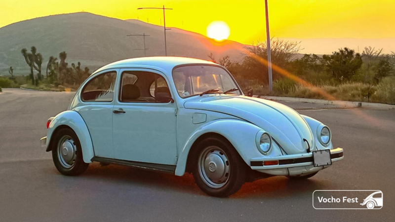 Volkswagen Vocho de color azul en un paisaje desértico al atardecer. 