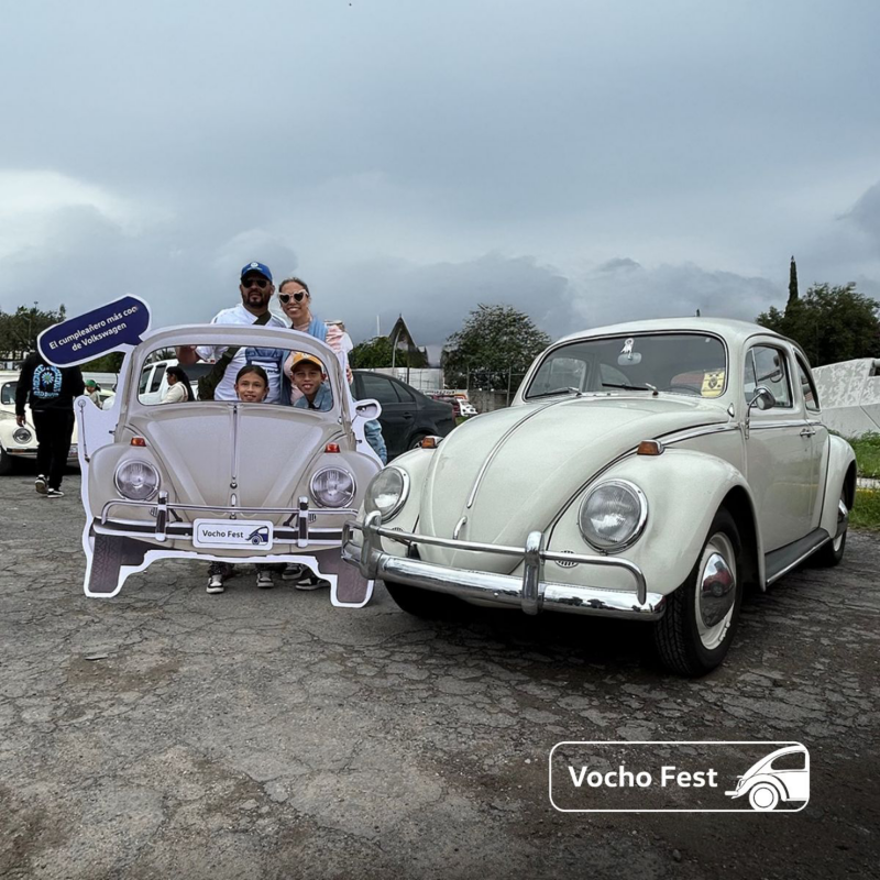 Asistentes al Vocho Fest en Puebla posan para una foto junto a un Vocho antiguo.