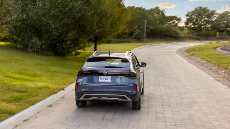 Volkswagen Nivus transita sobre avenida rodeada por área verde y árboles. 