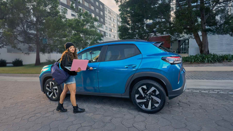 Mujer con laptop abre la puerta de conductor de Volkswagen Tera de color azul estacionado en la calle.