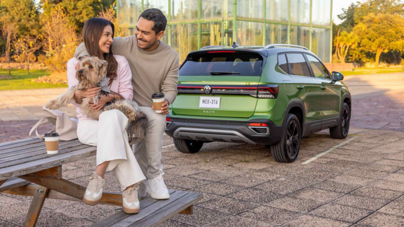 Pareja con un perro sentados sobre una mesa de campo con un Volkswagen Taos verde al fondo. 