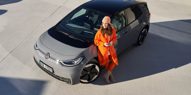 A woman with a smartphone in her hand is leaning against her grey VW ID.3