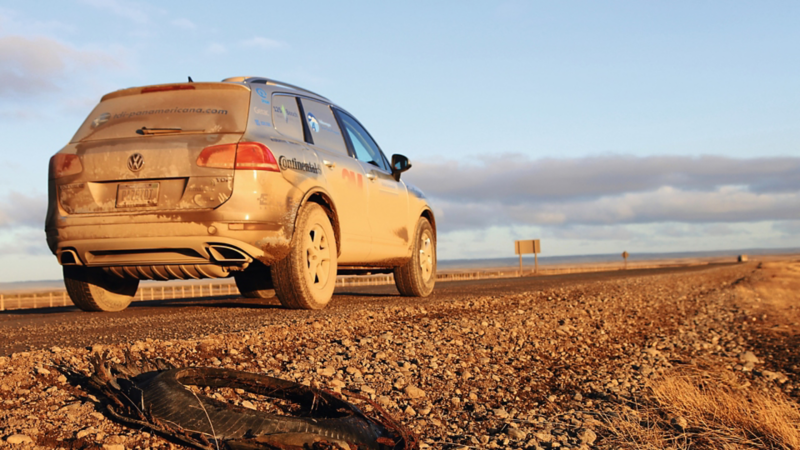 Un VW Touareg poussiéreux roule au soleil couchant sur une route isolée et rocheuse.