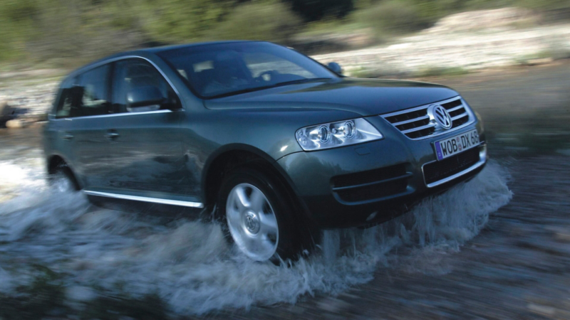 Un VW Touareg de première génération traverse dynamiquement des eaux peu profondes.