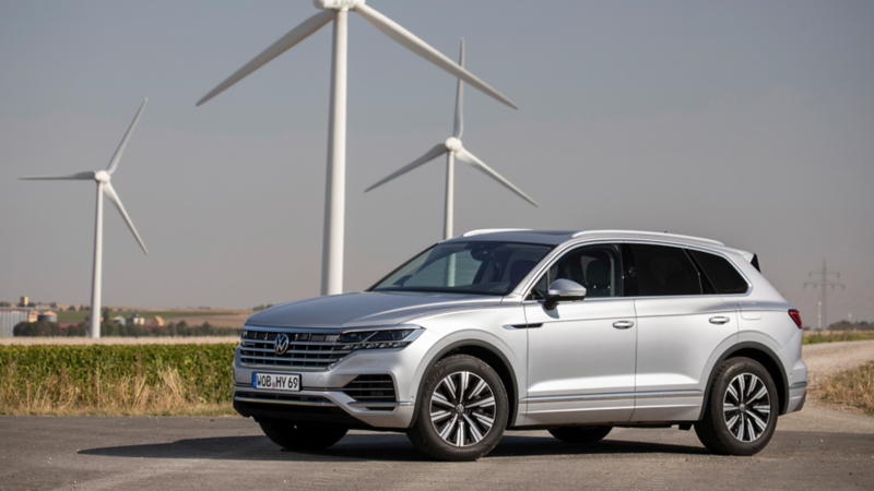 Un VW Touareg argenté de deuxième génération hybride devant des éoliennes.