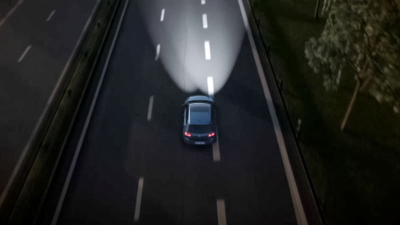 Car driving at night on an empty road with its headlights on