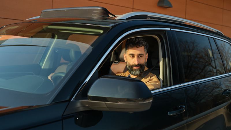 Un homme ayant sa ceinture attachée regarde par la fenêtre ouverte du côté conducteur d'un Atlas 2022 de Volkswagen noir profond nacré.