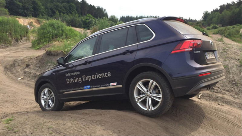 View of a Volkswagen Tiguan from behind and at an angle, driving over a hill on an unpaved road