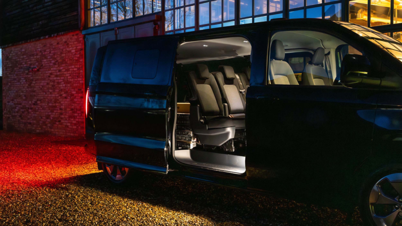 A black VW e-Transporter Kombi at night with its side doors opened and back lights on.