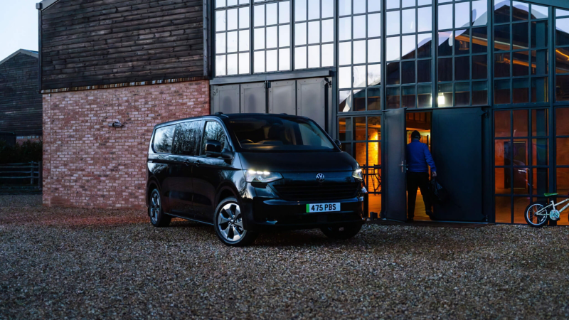 A black VW e-Transporter Kombi parked on gravelled grounds next to a building.