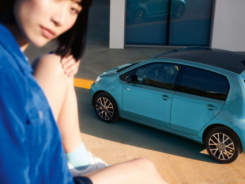 Eine Frau sitzt auf einer Mauer über einem geparkten e-up! und schaut in die Kamera