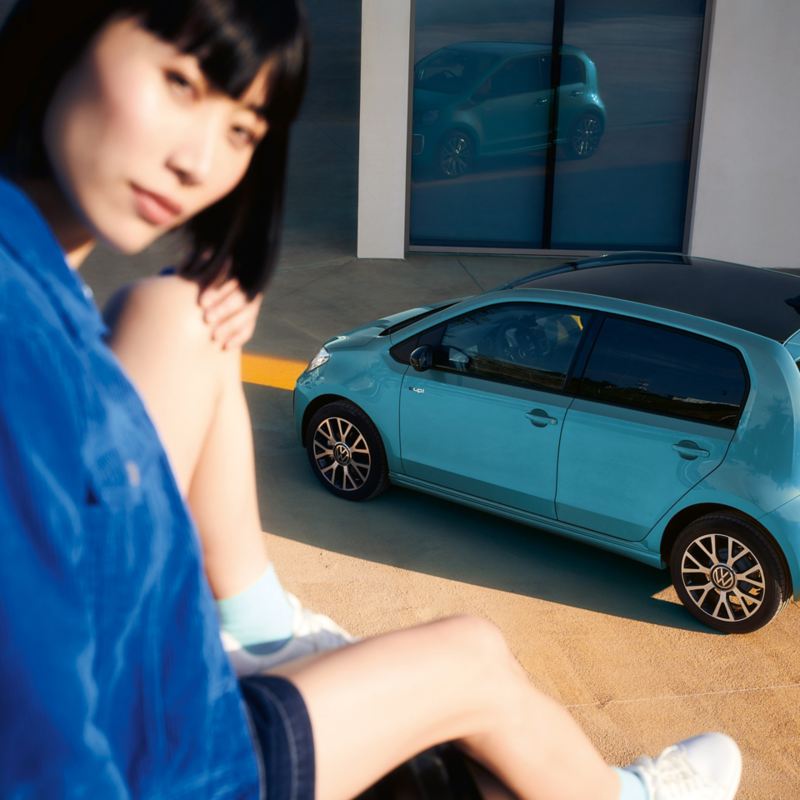 A woman sits on a wall above a parked e-up! and looks at the camera