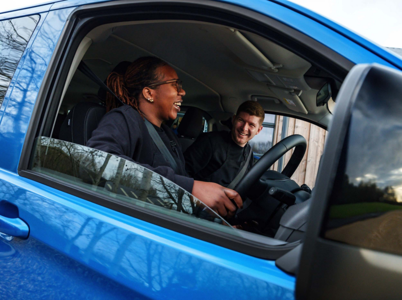 Two smiling people in the front seats of an e-Transporter van