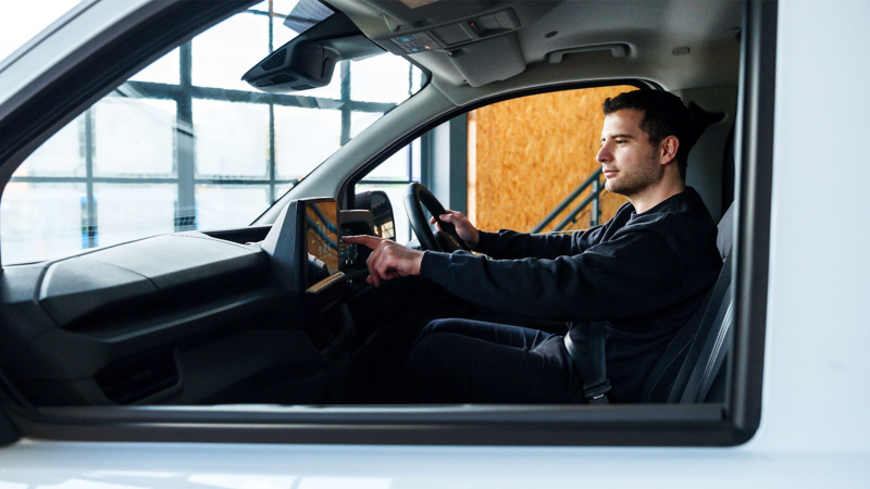 A man sat in the driving sear of an electric e-Transporter van and using the touchpad