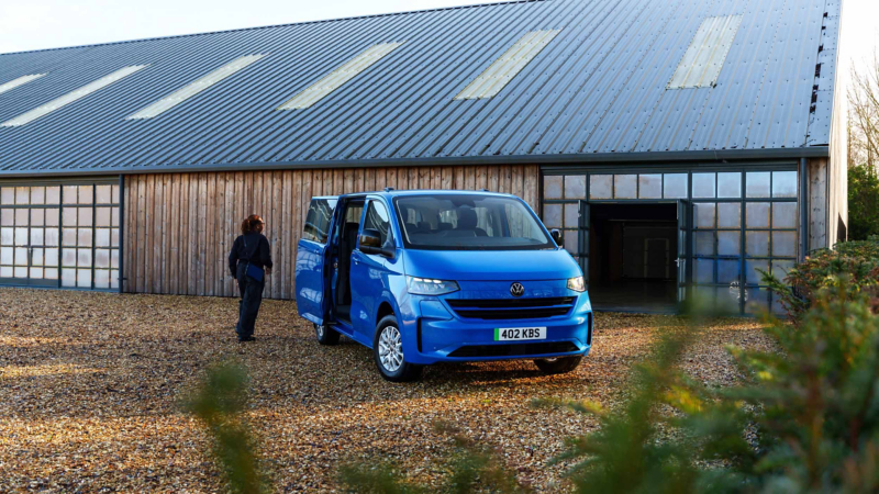 A woman walking towards a blue e-Transporter Shuttle van with its side door opened.