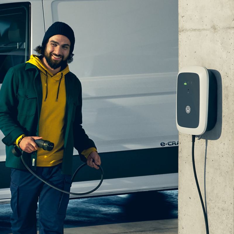 A Volkswagen ID. Charger on a concrete pillar and a man holding the charging cable.