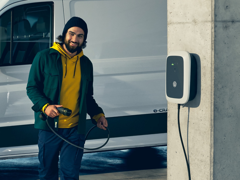 Un Volkswagen ID. Charger vicino a una colonna di cemento, un uomo tiene il cavo di ricarica. 