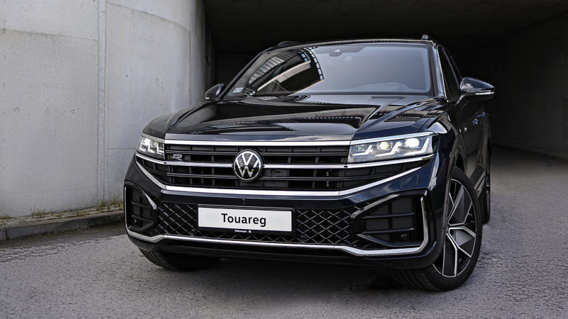 A VW Touareg R-Line parked at the roadside, diagonal view from above of the rear and panoramic sunroof.