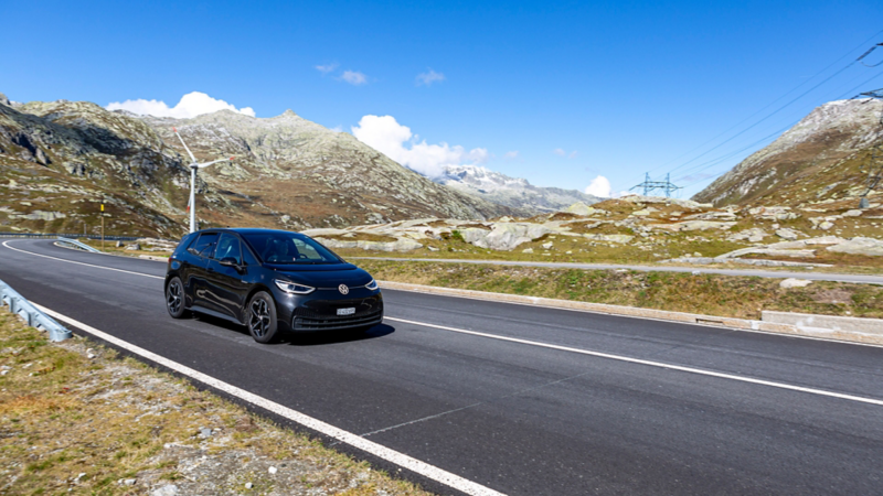 ID.3 fährt auf einer Pass-Strasse und im Hintergrund ist eine Windmühle und die Alpen