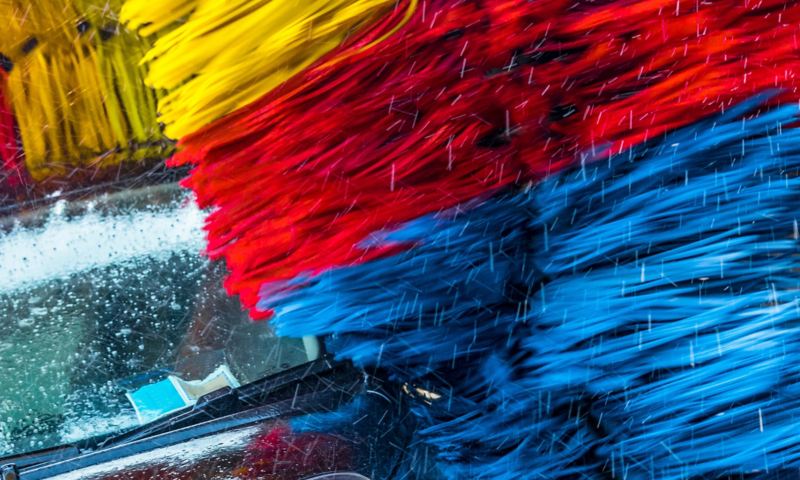 Ein Auto wird in einer automatischen Waschanlage von einer gelb-rot-blauen Bürste gereinigt.