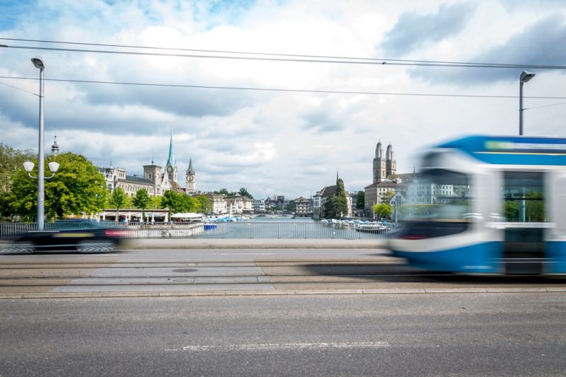 Ein blau-weißer Waggon der elektrisch betriebenen Straßenbahn fährt über eine Brücke in Zürich. 