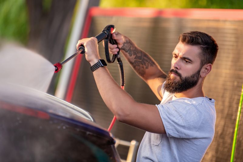 Ein Mann wäscht sein Auto in einer SB-Waschanlage mit einem Hochdruckreiniger.