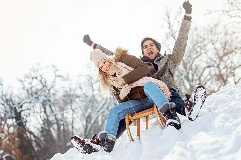 Ein Paar fährt mit einem Holzschlitten einen schneebedeckten Hang herunter.