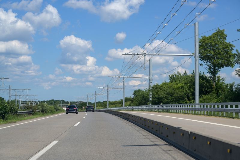 Eine Fahrbahn für Oberleitungskraftwagen führt rechts an zwei Pkw-Fahrstreifen einer Autobahn entlang.