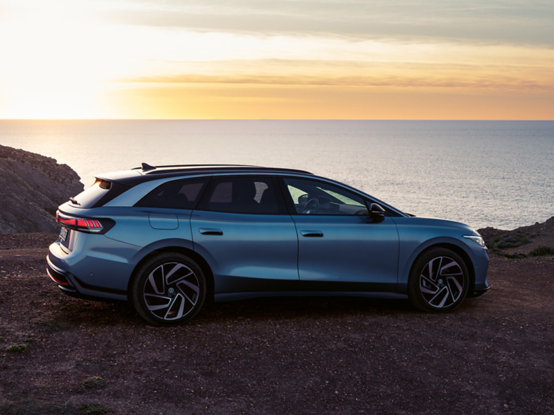 an ID7 Tourer parked by a beach with the sun setting in the background