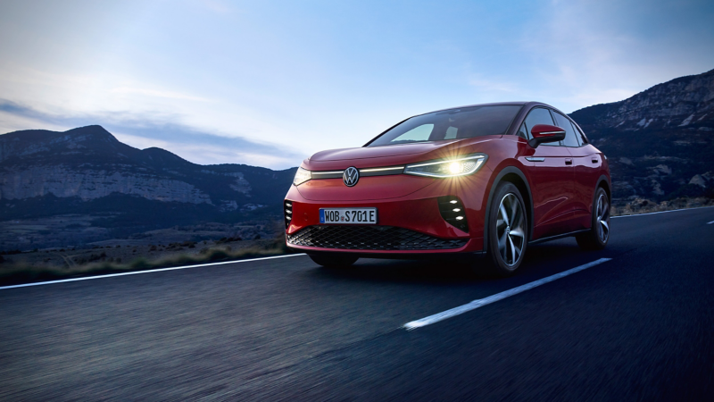 a red Volkswagen EV drinking along a road with a mountain range in the background