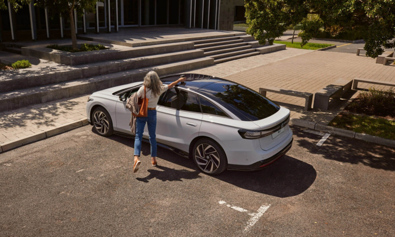 Photo showing a woman standing next to a parked VW ID.7. 