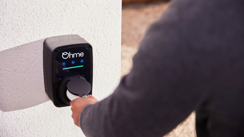 An Ohme walllbox device on a wall with man plugging in his charging cable