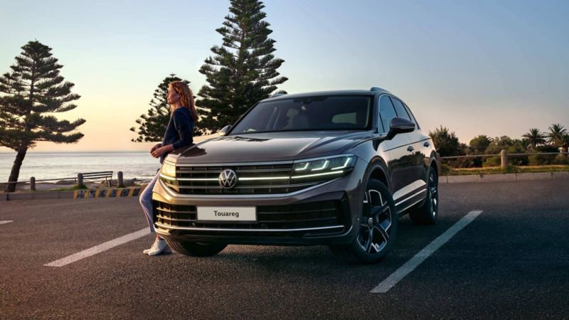 A new Touareg parked by the ocean with a woman leaning against the side of the car