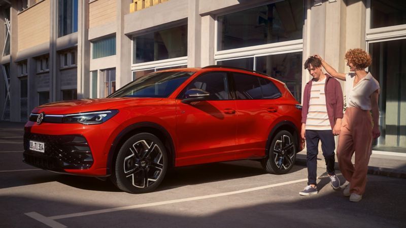 A new red Tiguan with a man and woman walking next to it